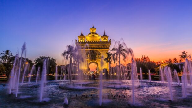 Sunset view of Vientiane with a golden monument and fountain in the foreground