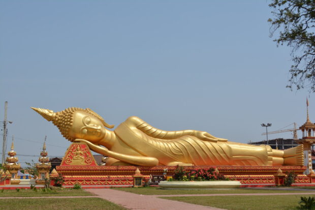 Reclining Buddha statue in Vientiane with clear sky and temple structures in the background