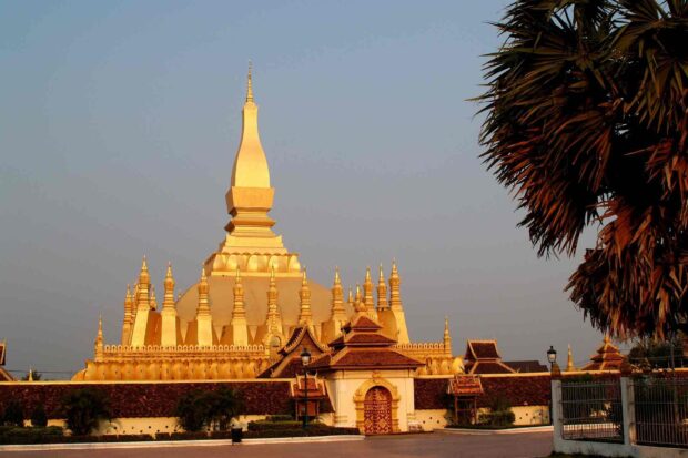The golden stupa in Vientiane surrounded by traditional architecture and palm trees