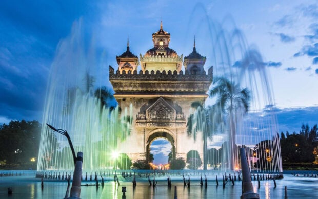 The Patuxai monument in Vientiane illuminated at dusk with water fountains in front