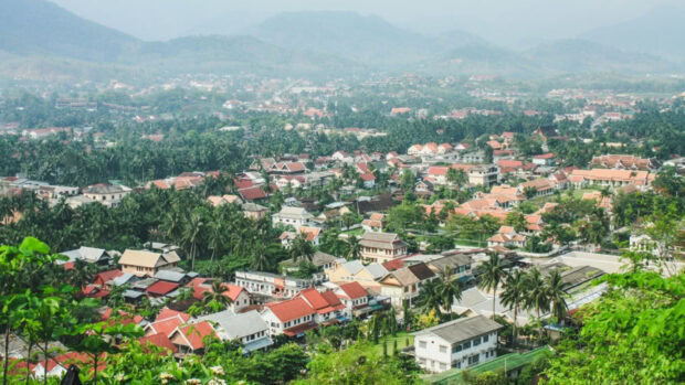 A panoramic view of Vientiane city with lush greenery and traditional houses in a valley surrounded by mountains