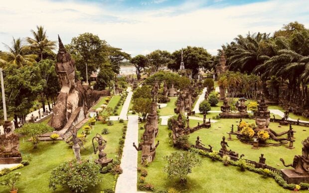 Ancient statues and sculptures in Vientiane garden with lush greenery and clear sky