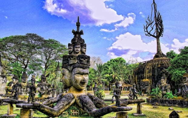 Stone sculptures with multiple faces and a symbolic tree in Vientiane park under a blue sky