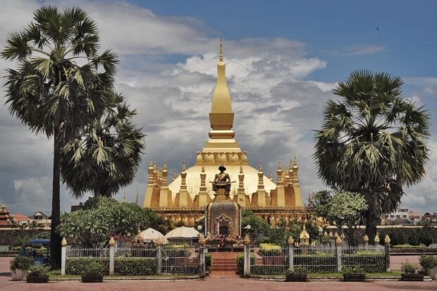 The golden stupa in Vientiane surrounded by palm trees and cloudy sky
