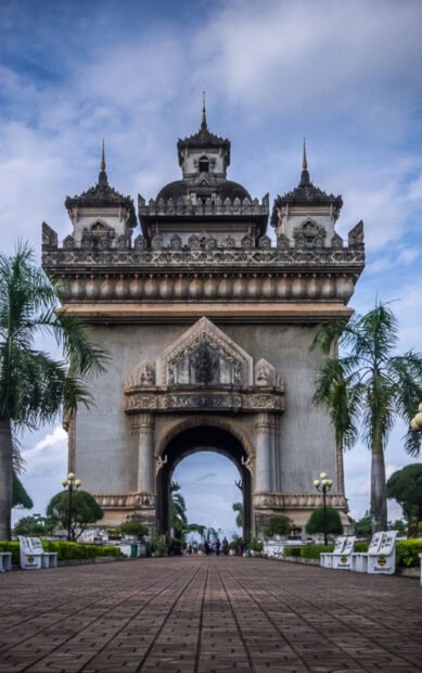 Historic arch monument in Vientiane with palm trees and cloudy sky