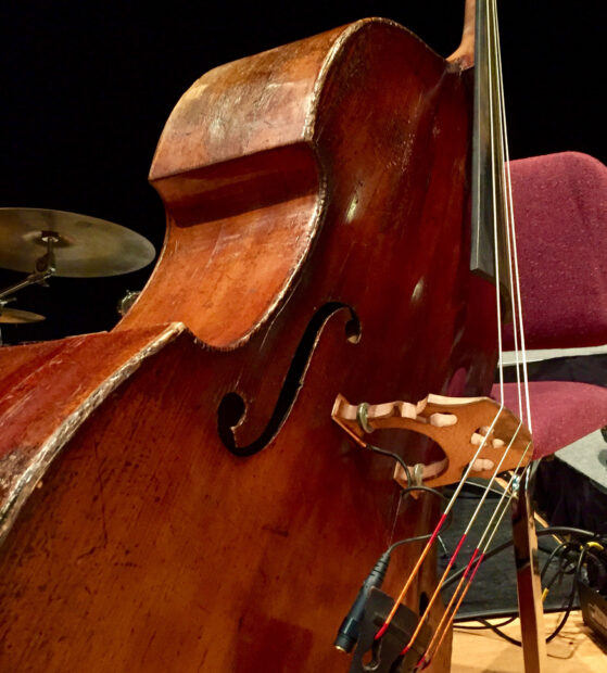 A vintage double bass with worn wood texture and strings resting near a purple chair, HD Desktop Wallpaper