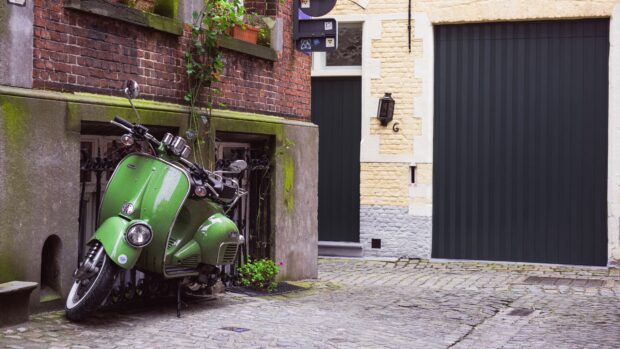 A green scooter is parked beside a mossy brick wall and cobblestone street, 4K Desktop Wallpaper