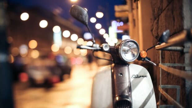 A close up of a vintage scooter on a wet street with blurred city lights in the background, 4K Desktop Wallpaper
