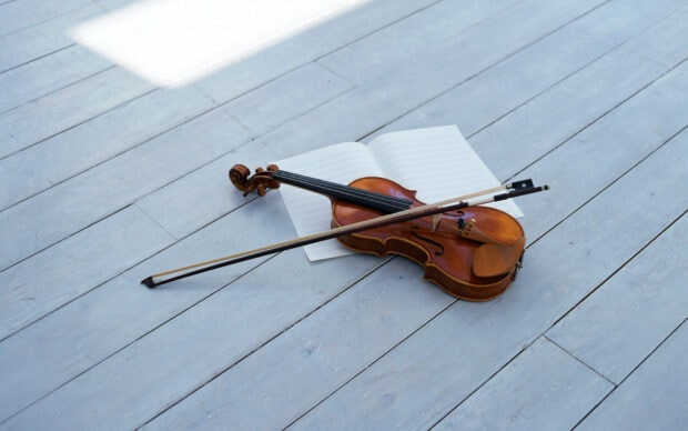 A violin and bow rest on a wooden floor next to open sheet music in a bright room, HD Desktop Wallpaper