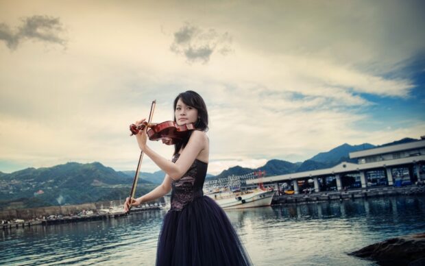 A woman plays violin outdoors near the harbor and mountains, HD Desktop Wallpaper