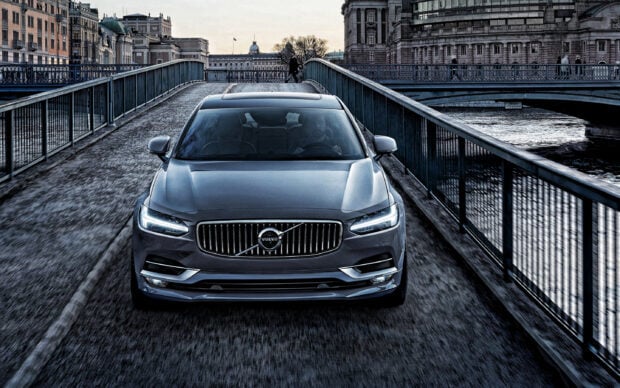A front view of a Volvo driving on a narrow bridge in an urban area
