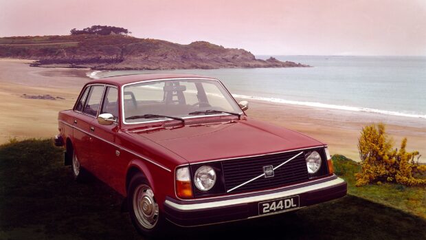 Classic red Volvo sedan parked near the ocean with a rocky coastline in the background