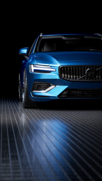 Blue Volvo front view with modern headlights on reflective floor in dark setting