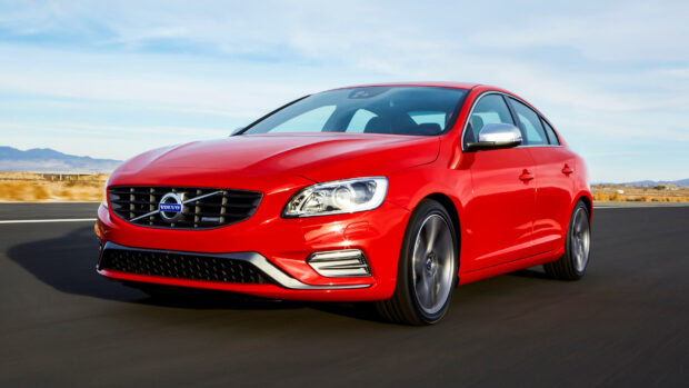 Red Volvo driving on a road with mountains in the background