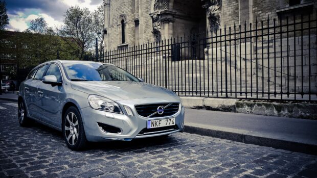 Silver Volvo car parked on a cobblestone street near a historic building with stairs and iron fence