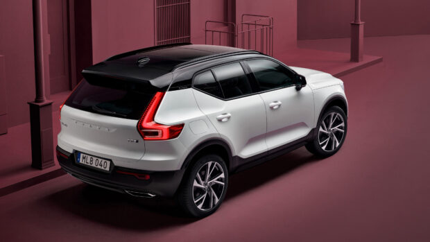 A white Volvo XC40 with a black roof is parked in a maroon colored urban setting