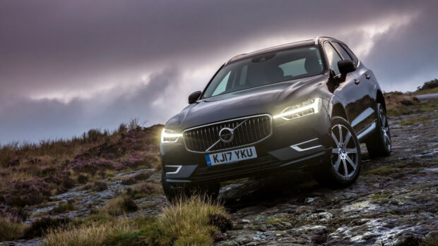 Black Volvo car driving on rocky terrain with cloudy sky in the background