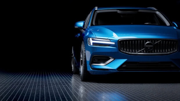 Blue Volvo car front side view with illuminated headlights on reflective grid floor