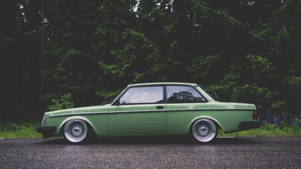 Classic Volvo car in green color parked on road with forest background