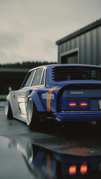 Blue Volvo car with rotiform decal parked outside industrial building on wet ground