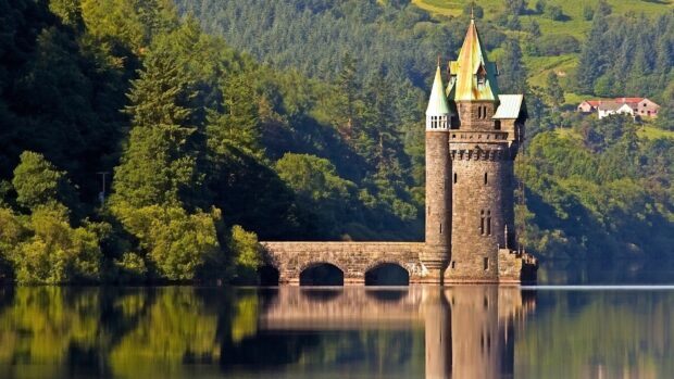 A historic castle stands by a calm lake with lush green trees in Wales, HD Desktop Wallpaper