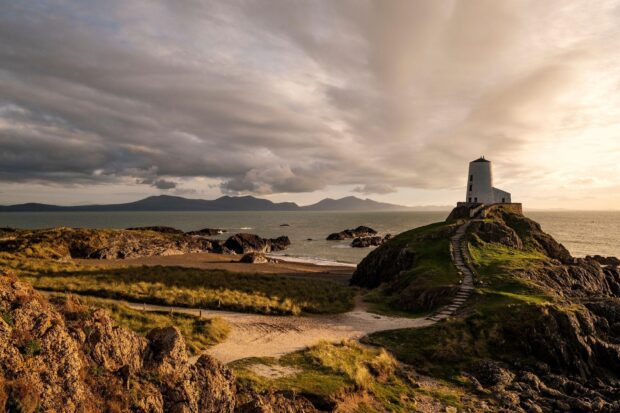 A scenic view of Wales with a lighthouse on the rocky coast under a cloudy sky, HD Desktop Wallpaper