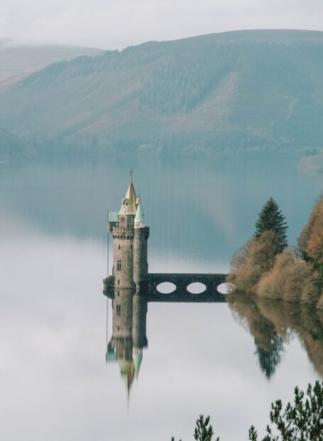 A serene castle rises from calm waters surrounded by hills in Wales Wallpapers, HD Phone Wallpaper
