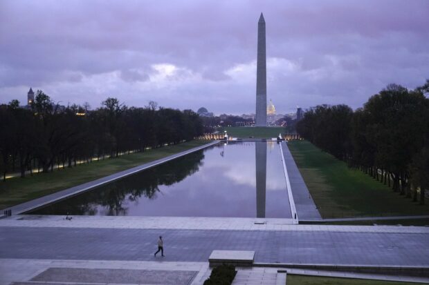 A calm view of the Washington Monument reflecting in the pool surrounded by trees at dusk