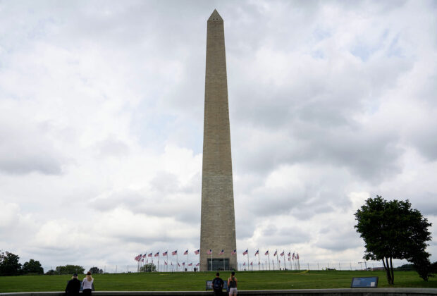 The Washington Monument stands tall surrounded by flags on a cloudy day at the national mall