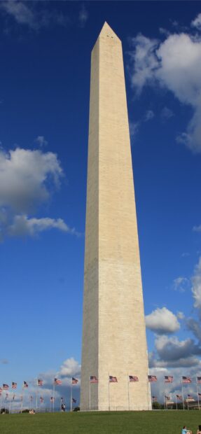 The Washington Monument stands tall under a partly cloudy sky with American flags surrounding the base