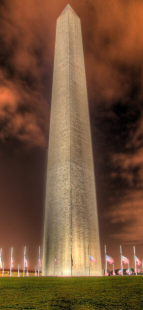 Illuminated Washington Monument structure at night with American flags surrounding it