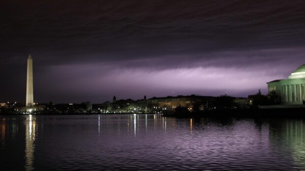 Washington Monument stands tall near the water at night under a cloudy purple sky