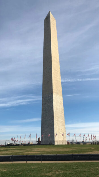 Washington Monument stands tall against a clear blue sky with American flags surrounding the base