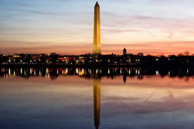 Washington Monument towering over the cityscape reflected in the calm water at sunset