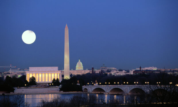 The Washington Monument stands tall at night with a full moon in the sky