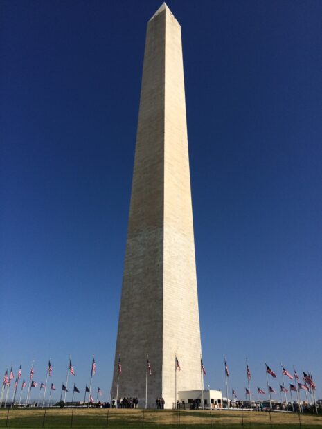 The Washington Monument stands tall surrounded by multiple American flags in clear daylight