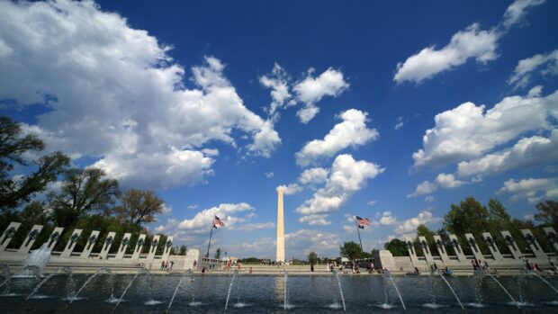 The Washington Monument stands tall under a blue sky with scattered clouds and American flags displayed