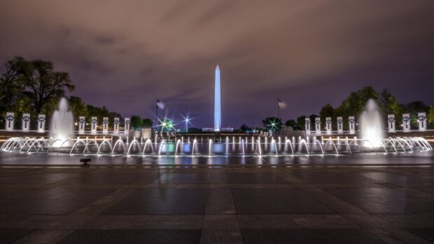 Washington Monument illuminated at night with water fountains in the foreground and clear dark sky