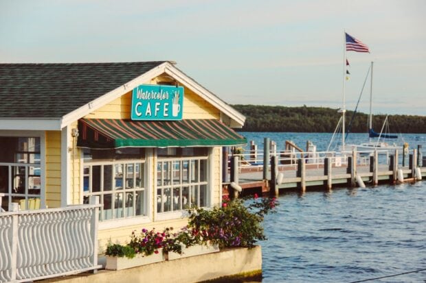 A yellow watercolor cafe sits by the water with boats and an American flag at Mackinac Island, HD Desktop Wallpaper