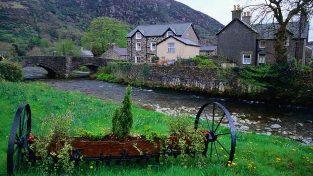 A scenic view of the Welsh countryside featuring a stone bridge over a flowing river and traditional houses, HD Desktop Wallpaper