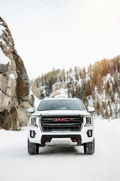A white GMC truck is parked on a snowy road near rocky cliffs and pine trees, 2K Phone Wallpaper