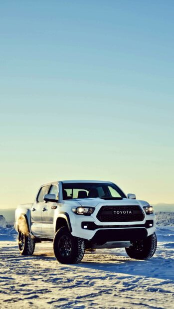 Snow-covered off-road vehicle in a winter landscape with clear sky and mountains in the background.