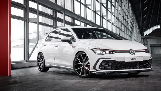 A white Volkswagen Golf GTI is parked inside a spacious industrial garage with glass windows, 2K Desktop Wallpaper