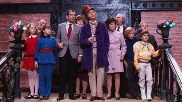 Willy Wonka standing with a group of people in a colorful setting from the movie Willy Wonka
