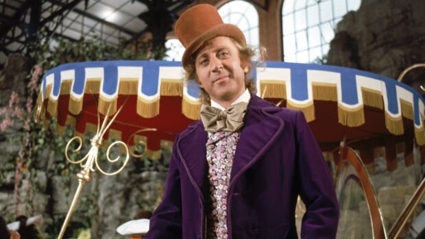 A man wearing a purple suit and brown top hat representing Willy Wonka in a colorful setting