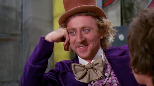 Willy Wonka smiling in a purple coat and brown top hat with a large bow tie
