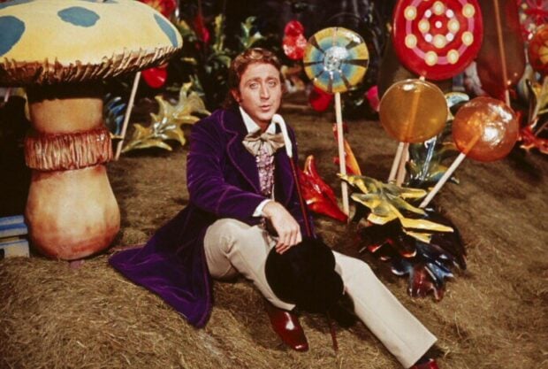 A man dressed as Willy Wonka sitting among giant candy and oversized mushrooms