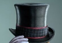 A close up of Willy Wonka wearing a top hat and purple glove
