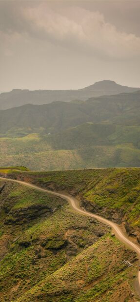A winding road leads through lush green hills in Ethiopia under a cloudy sky, 2K Mobile Wallpaper