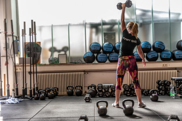 A woman is lifting a dumbbell during a Crossfit workout in a gym full of weights, HD Desktop Wallpaper